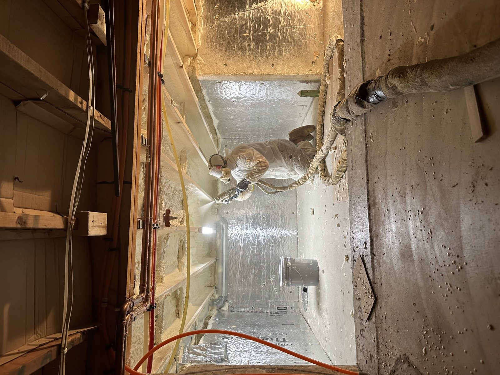 Installer spraying foam insulation into a building cavity